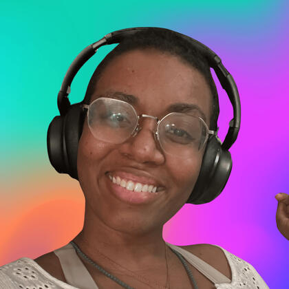 Headshot of TylerVoiceActs Photo of TylerVoiceActs, Medium Dark Skinned Femme with short shaved black hair and thin metal octagonal glasses smiling with black over the ear headphones on a multicolored teal, orange, and magenta background.